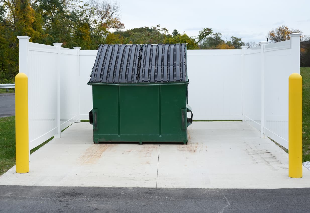 Clean green dumpster in a white vinyl enclosure on a tidy concrete pad